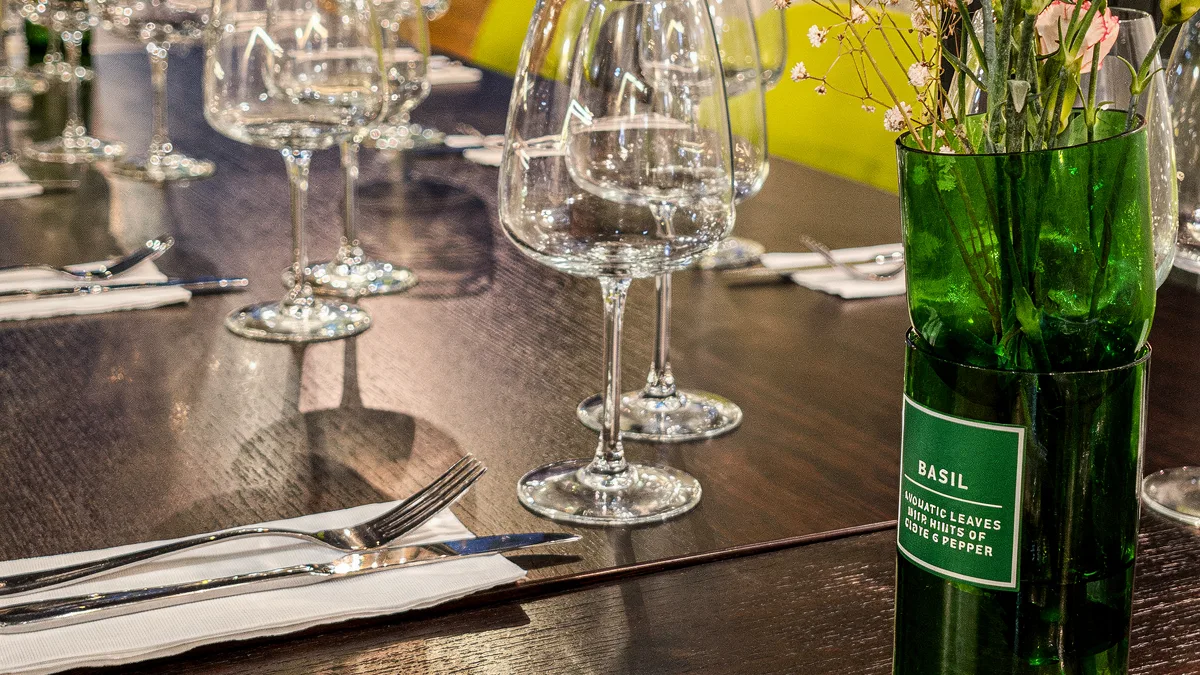 A set table with wine glasses and a BASIL vase