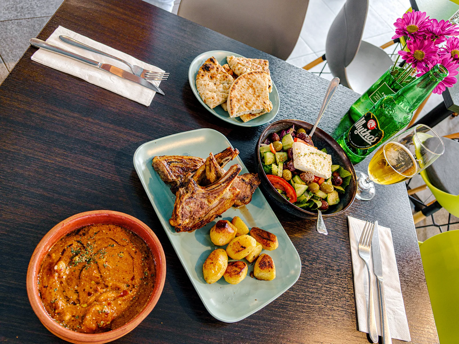 Lamb chops, Greek salad, pita and Mythos on the table